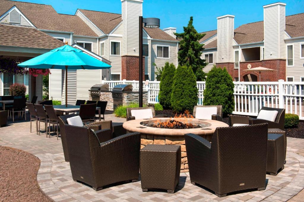 a patio with a fire pit and chairs and an umbrella at Residence Inn Syracuse Carrier Circle in East Syracuse