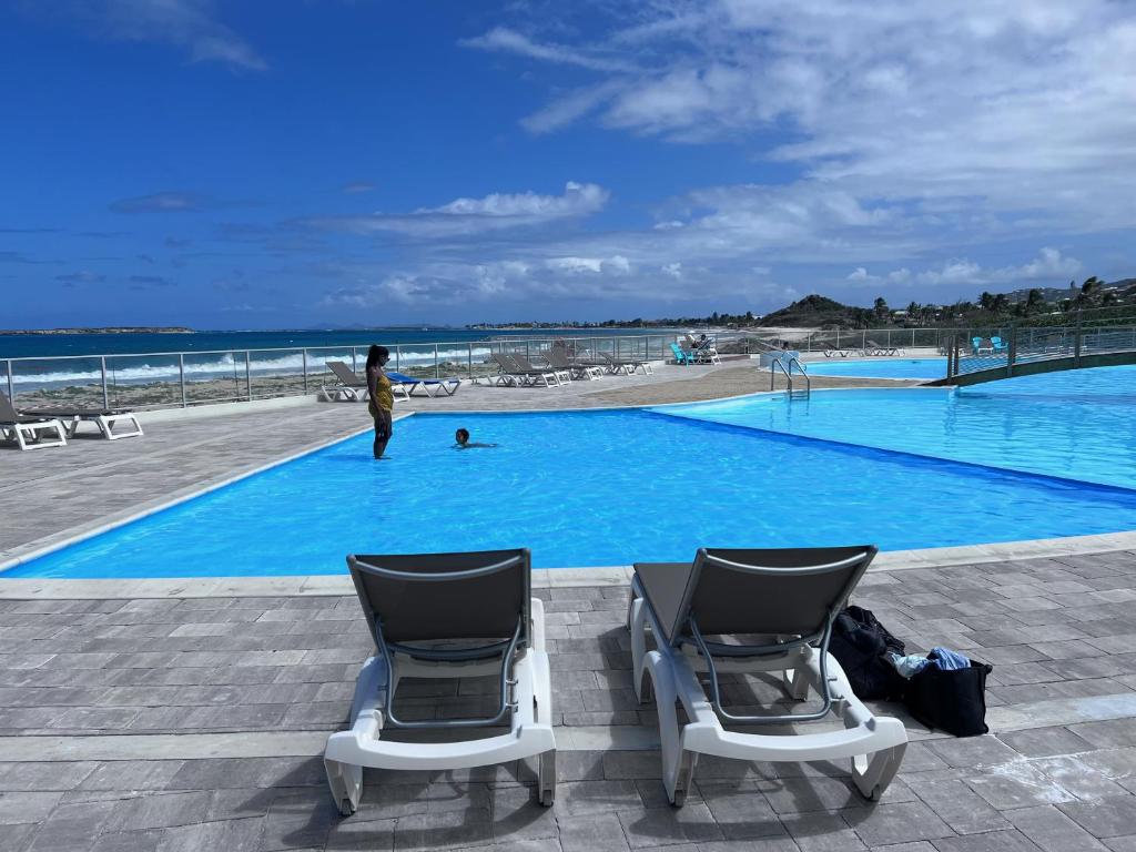 duas cadeiras sentadas ao lado de uma piscina ao lado da praia em Studio Tortola Orient Bay VUE MER em São Martinho