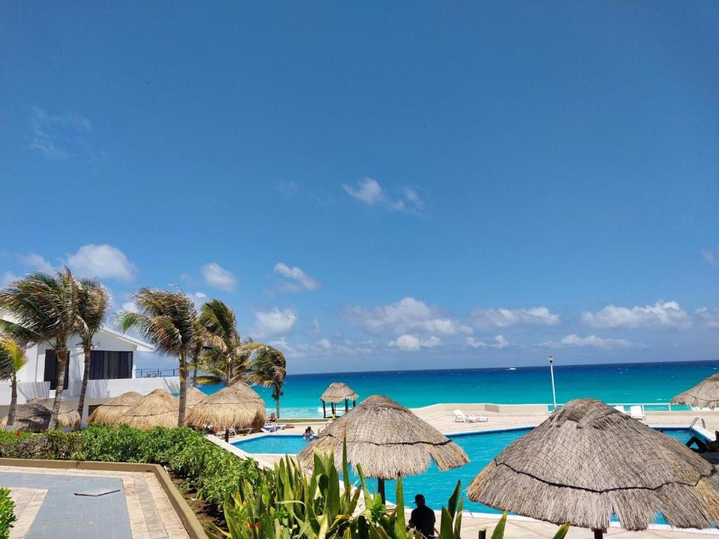 un complejo con piscina y algunas sombrillas de paja y el océano en Placentero depa en mar caribe!, en Cancún