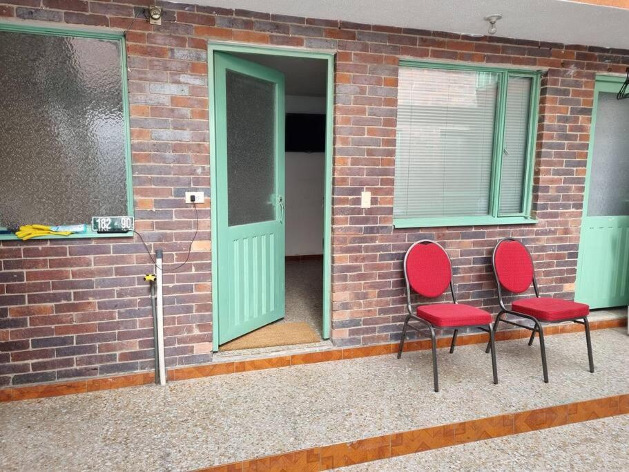 two red chairs sitting next to a brick wall with a door at Aparta estudio bonito, independiente bien ubicado in Bogotá