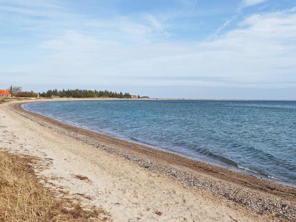 una playa de arena con agua y árboles a lo lejos en Holiday home Lemvig XLII, en Lemvig