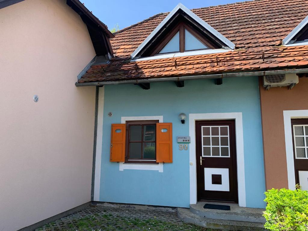 una casa azul y blanca con una puerta naranja en Lotty en Čatež ob Savi
