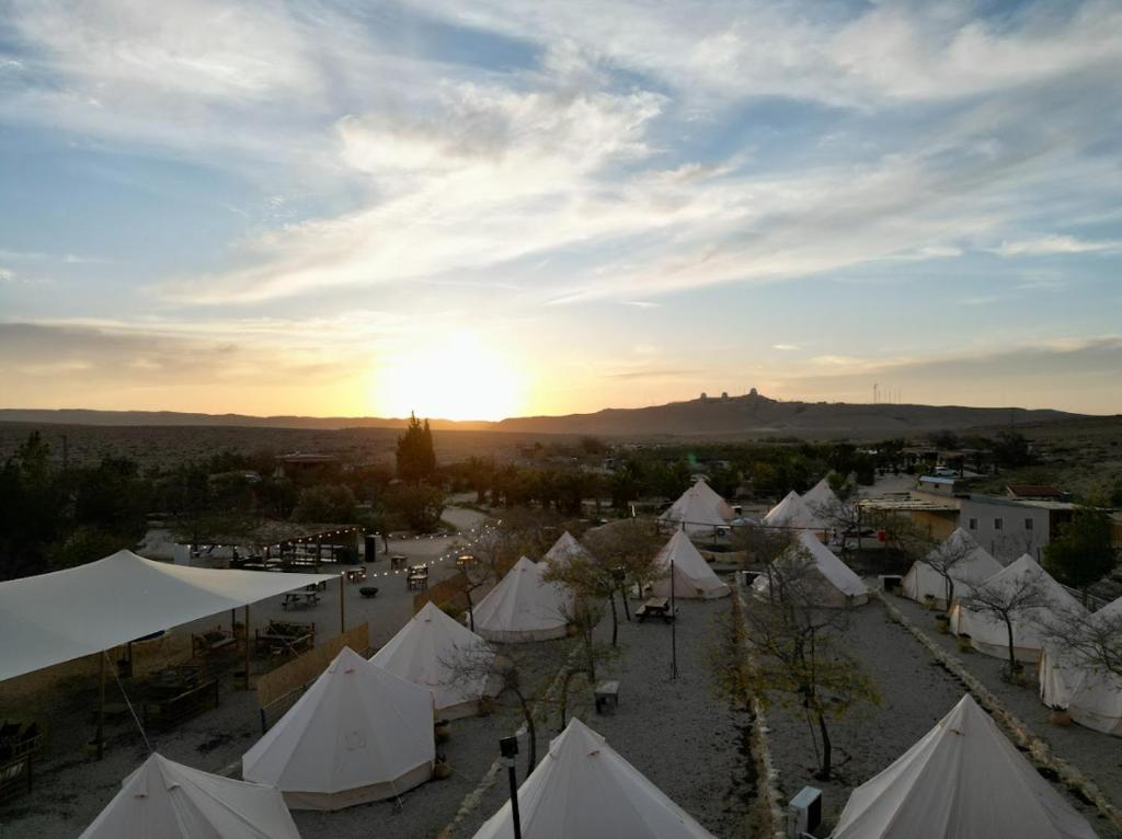 - un groupe de tentes blanches avec le coucher du soleil en arrière-plan dans l'établissement KARMEI NEGEV - מתחם גלמפינג ואטרקציות מבית גלובל גלמפינג, à Mitzpe Ramon