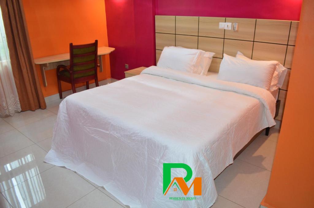 - une chambre avec un grand lit blanc et une chaise dans l'établissement RESIDENCES MICKEL, à Yaoundé