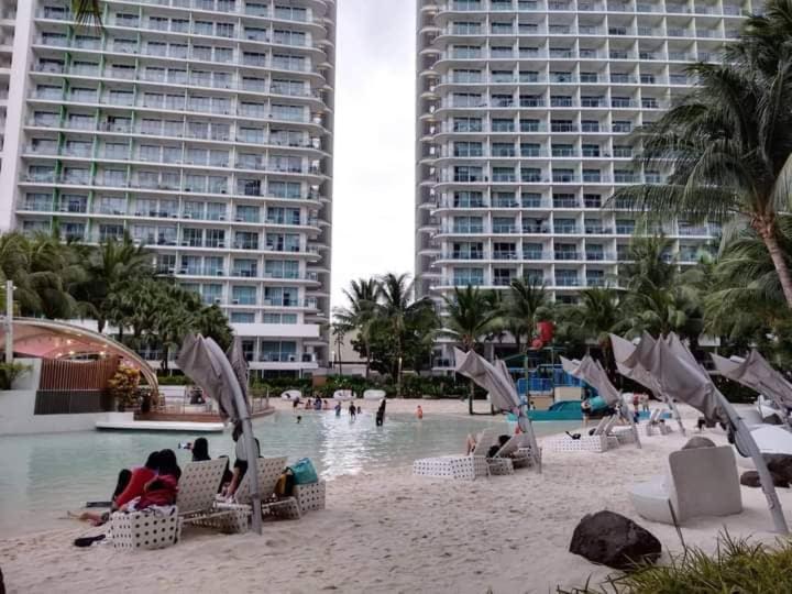 einen Strand mit Stühlen und Menschen im Wasser und in den Gebäuden in der Unterkunft Azure Staycation with wavepool & white sand beach in Manila