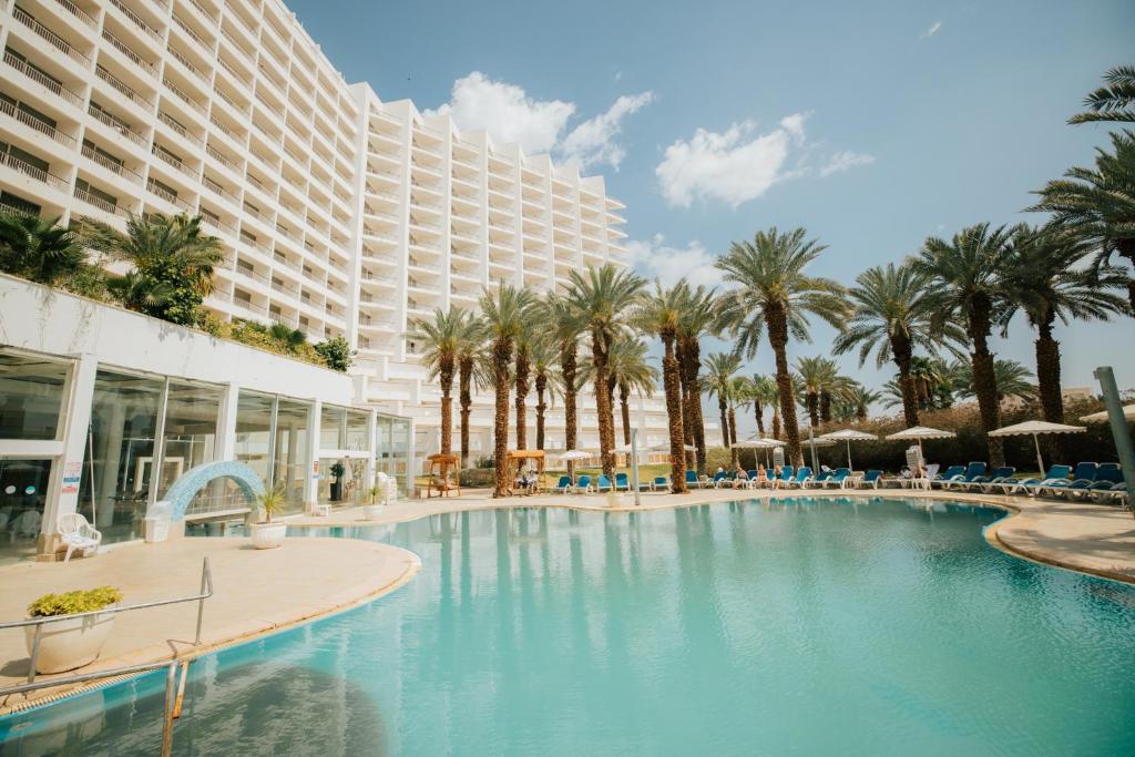 a large swimming pool with palm trees and a large building at David Dead Sea Resort & Spa in Ein Bokek