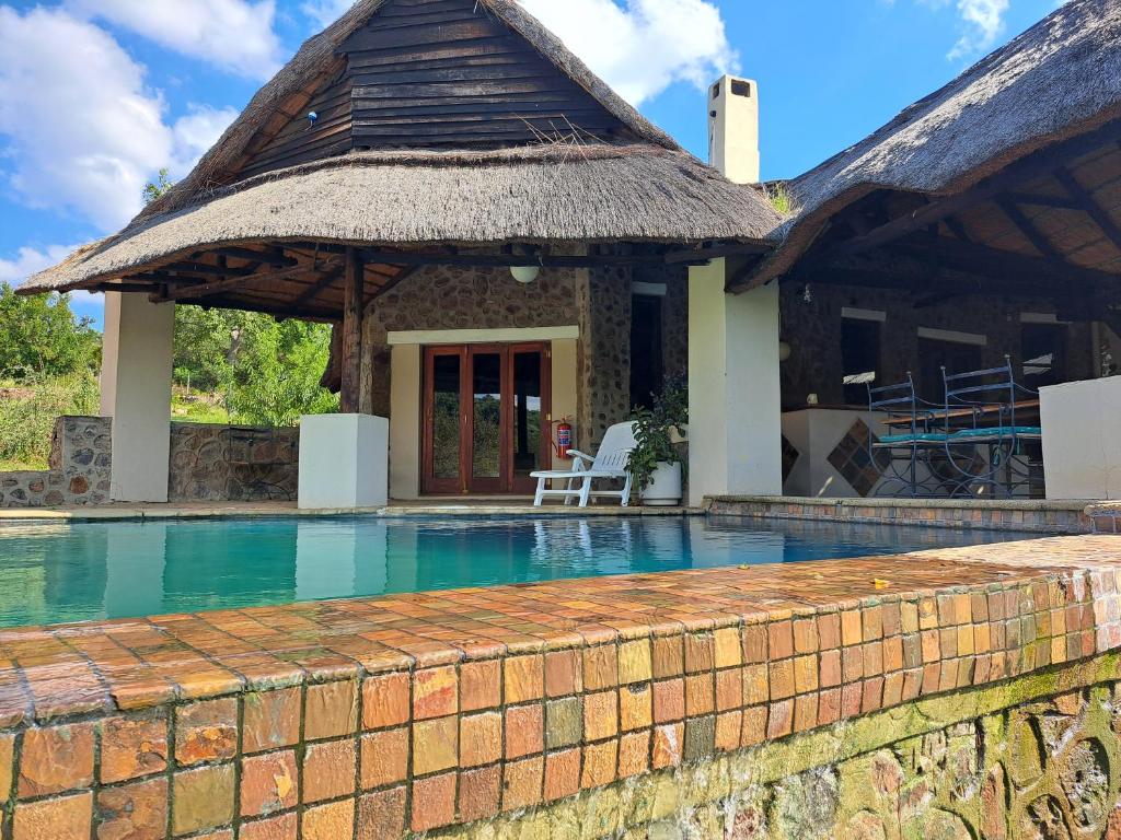 a house with a swimming pool with a thatch roof at Stone Meadows Country Estate-NV51 in Magaliesburg