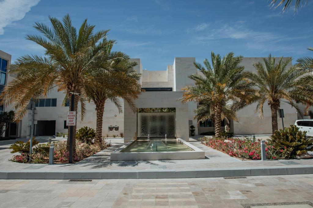 a building with palm trees in front of a fountain at Alberni Jabal Hafeet Hotel Al Ain in Al Ain