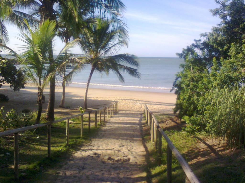 un chemin menant à une plage avec des palmiers et l'océan dans l'établissement Pousada Enseada do Coqueiro, à Guarapari