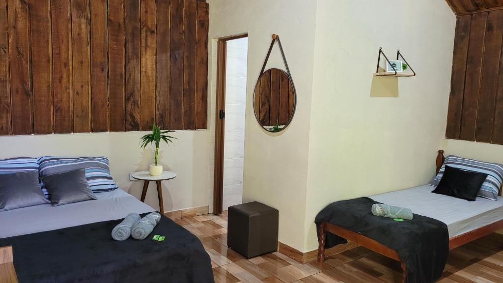 a bedroom with two beds and a table and a mirror at Chalé Recanto da Cachoeira I in Eldorado
