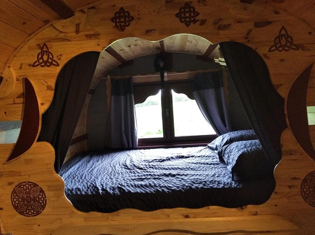 uma cama num chalé de madeira com uma janela em Roulotte irlandaise Polly em Saint-Vincent-en-Bresse