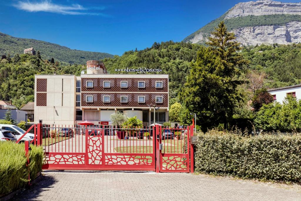 um portão vermelho em frente a um edifício com uma montanha em Hôtel Les Trois Roses, Meylan Grenoble The Originals Boutique em Meylan
