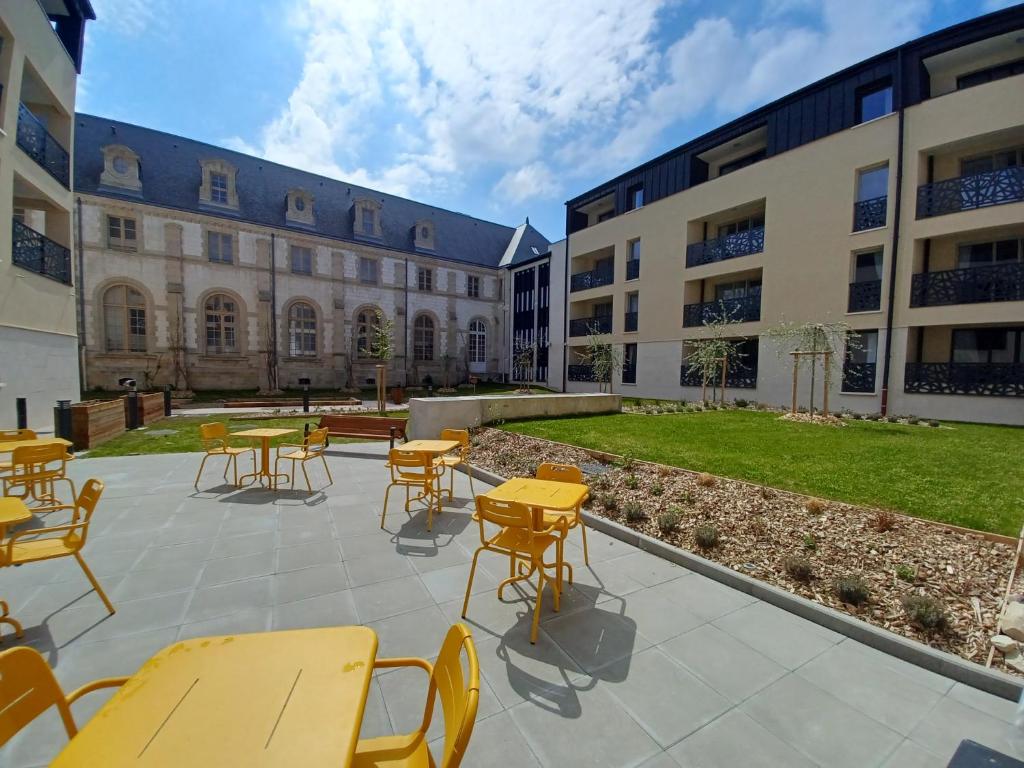 une cour avec des tables et des chaises devant un bâtiment dans l'établissement Domitys La Clef des Arts, à Châlons-en-Champagne