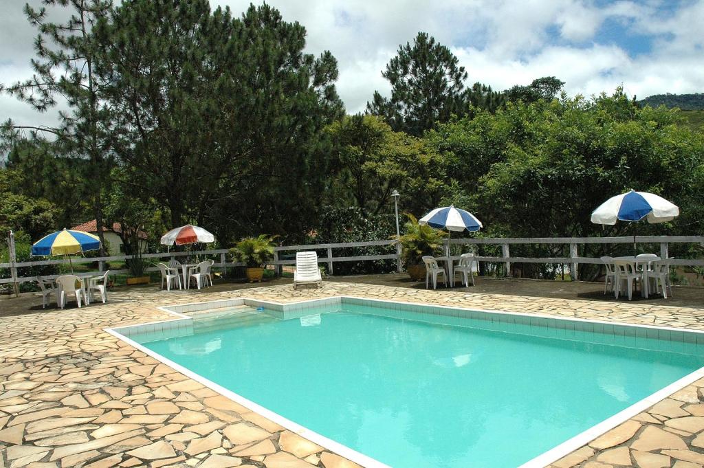 a swimming pool with tables and chairs and umbrellas at Pousada & Camping Serras Verdes in Conservatória