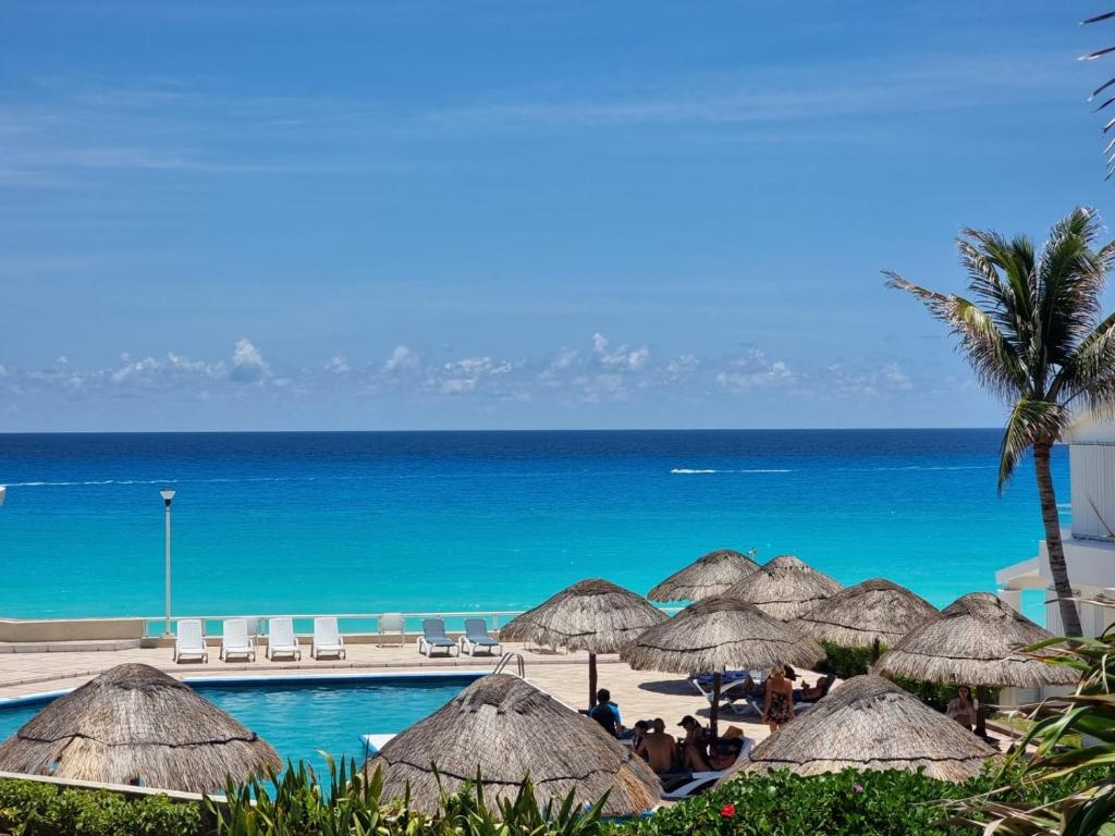 una piscina con sombrillas de paja y el océano en Suite Brisas Cancun, en Cancún