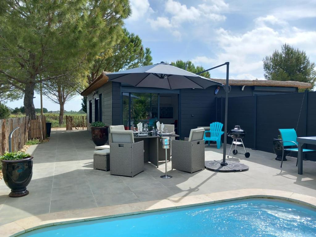 - une terrasse avec une table et un parasol à côté de la piscine dans l'établissement Domaine de L'Outarde Canepetiére Gîte A, à Aigues-Mortes