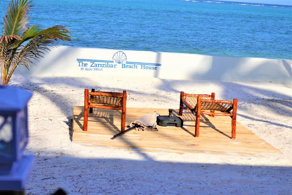 two benches on a beach next to the ocean at The Zanzibar Beach House-West in Pingwe