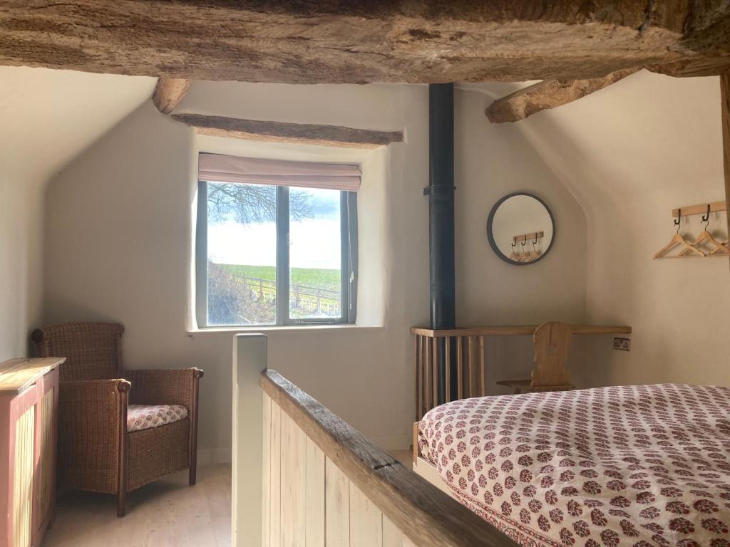 1 dormitorio con cama, ventana y silla en Whichford Mill Barn- Soulful retreat., en Shipston on Stour