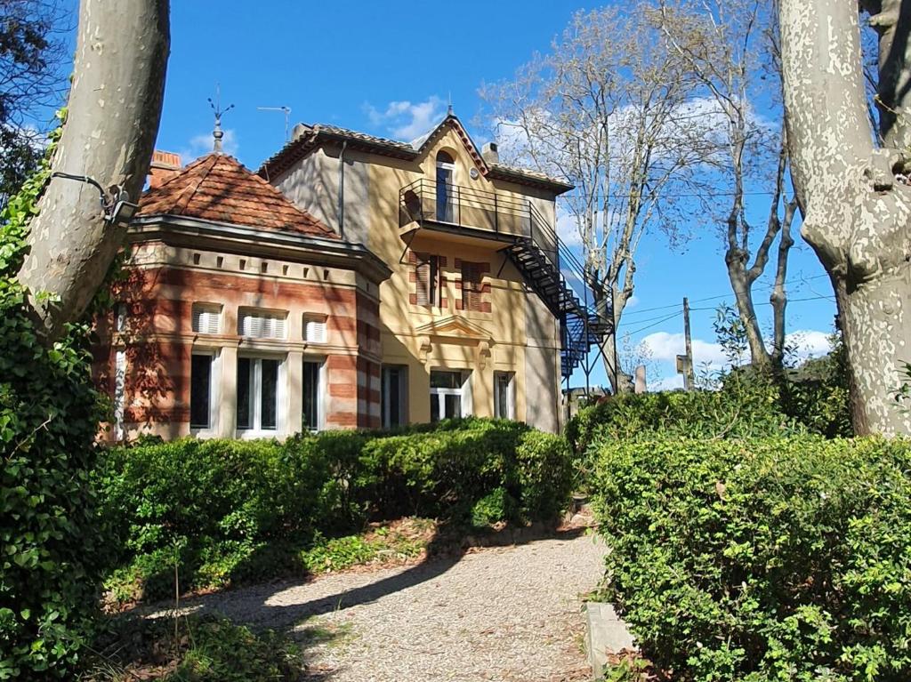 una vieja casa de ladrillo con arbustos delante de ella en Gîte du parc à Langel, en Armissan