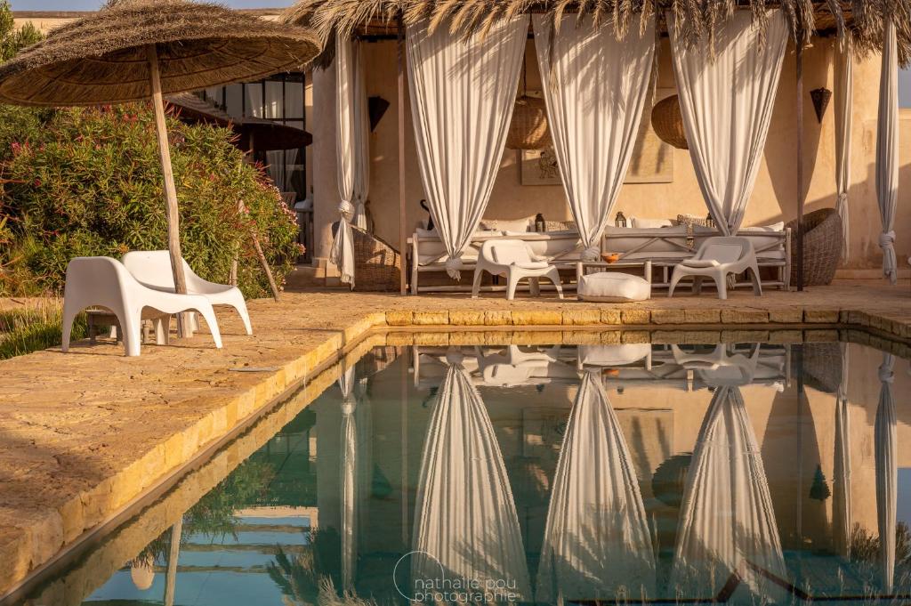 a pool with chairs and umbrellas next to a hotel at Dar Alya Essaouira Maison et table d'hôtes in Ghazoua