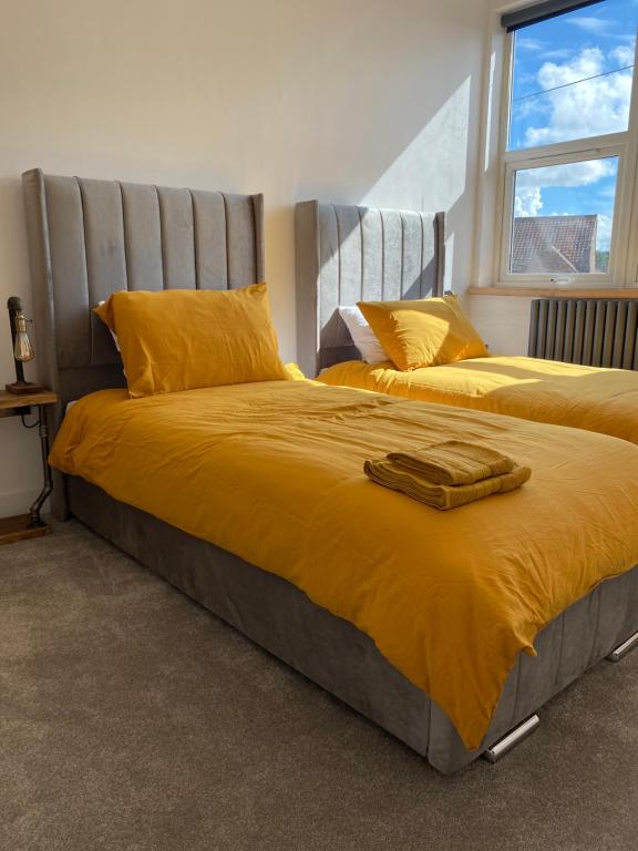 a bedroom with two beds with yellow sheets and a window at Stylish 2 Bed Apt, 2 Minute Walk From The Beach. in Sheringham