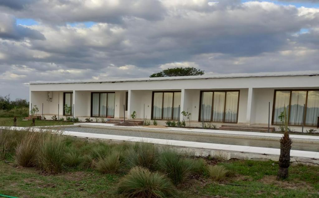 a white building with large windows on a field at Casimiro Ibera Hotel Boutique in Colonia Carlos Pellegrini