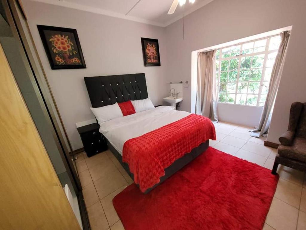 a bedroom with a bed with a red blanket and a window at Van Buuren Lodge in Germiston