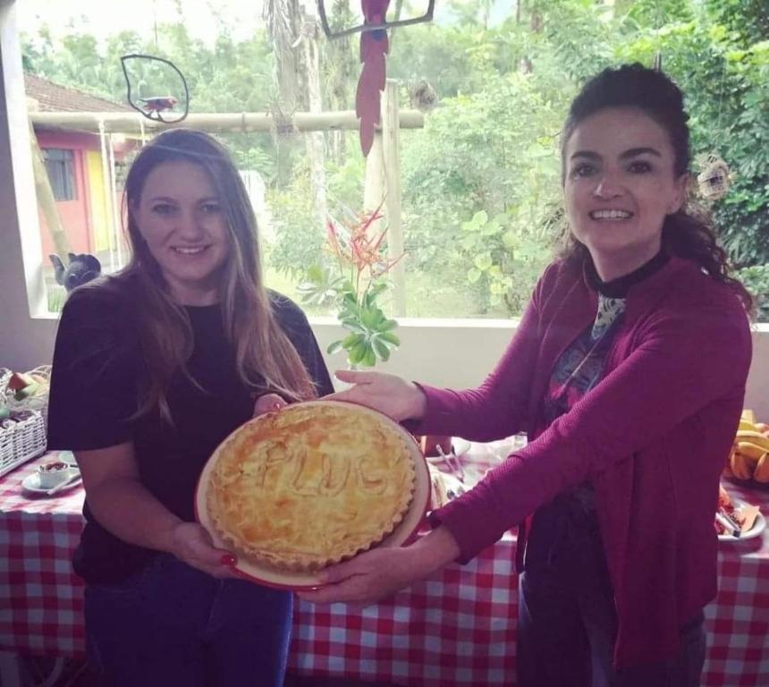 Duas mulheres estão a segurar uma tarte em frente a uma mesa. em Pousada do colono em Morretes