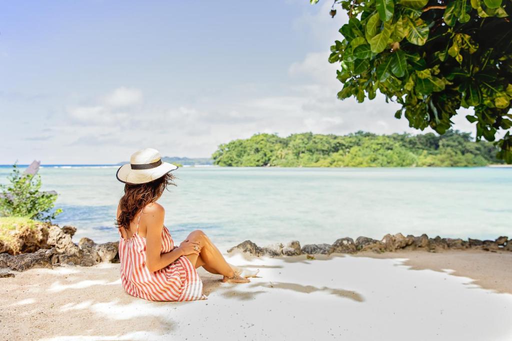 een vrouw in een gestreepte jurk en hoed zittend op een strand bij Turtle Bay Lodge in Luganville