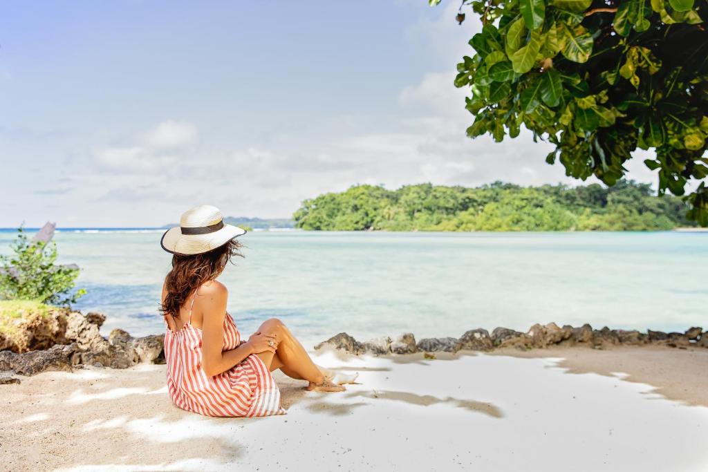 Una mujer con un vestido de rayas y sombrero sentada en una playa en Turtle Bay Lodge, en Luganville