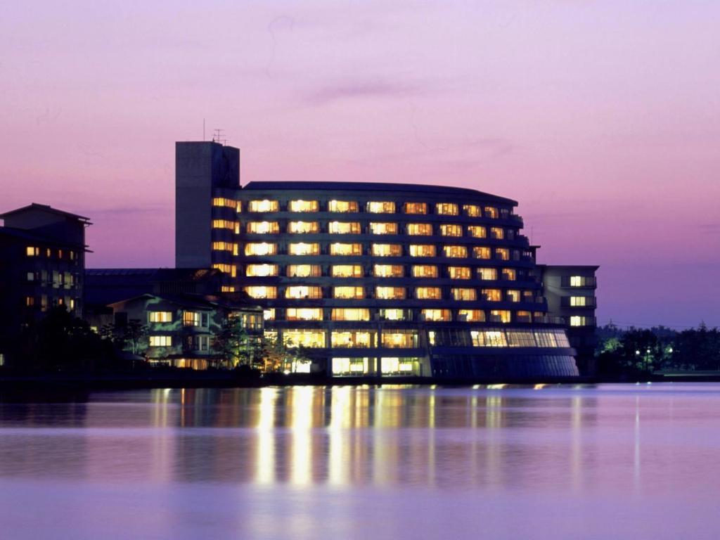 un edificio con luces encendidas en el agua por la noche en Kaga Katayamazu Onsen KASUIKYO (APA HOTELS & RESORTS), en Kaga