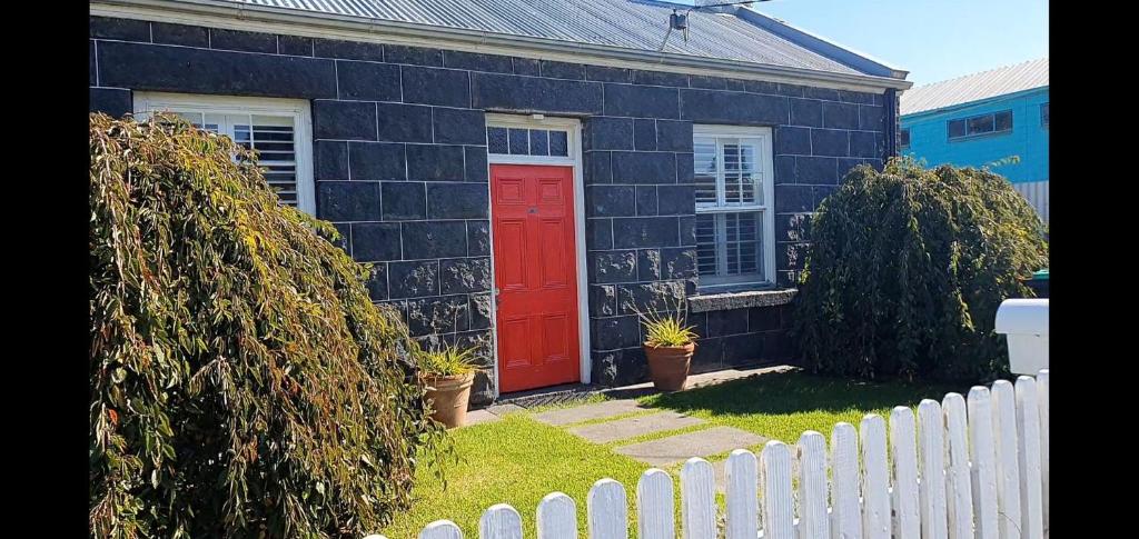 a red door on a black house with a white fence at Youngs Cottage in Port Fairy