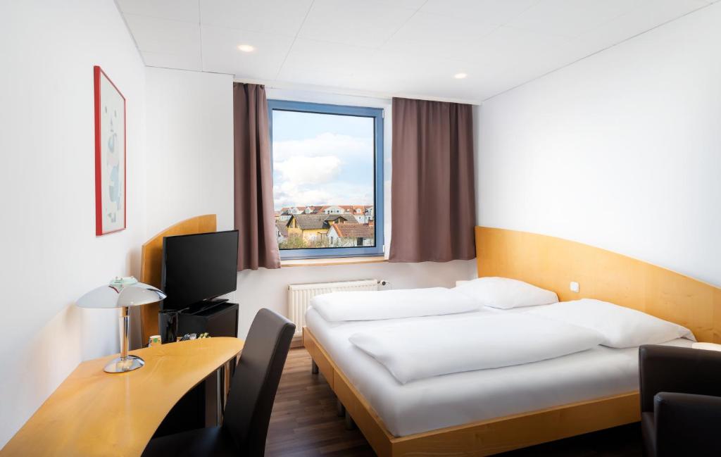 a hotel room with a bed and a desk and a window at Mainstreet Hotel in Dietzenbach