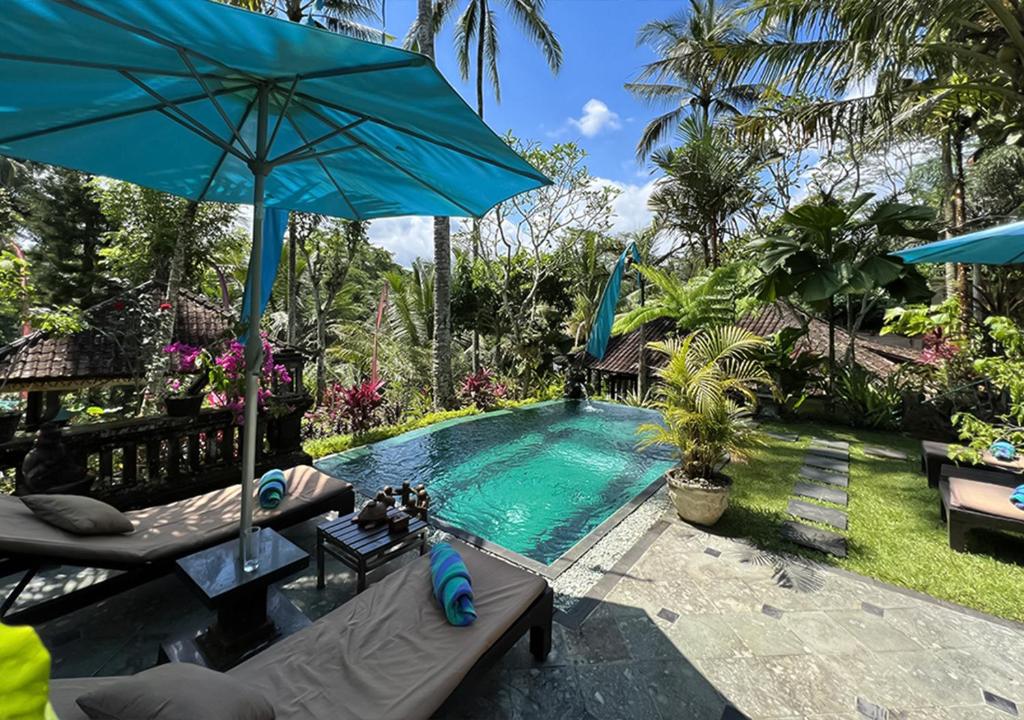 una piscina con una sombrilla azul y una mesa en The Mahogany Villa, en Tegalalang