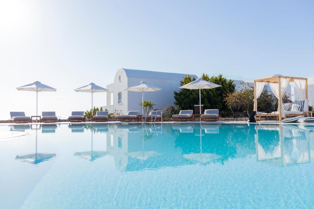 a large swimming pool with chairs and umbrellas at Astro Palace Hotel & Suites in Fira