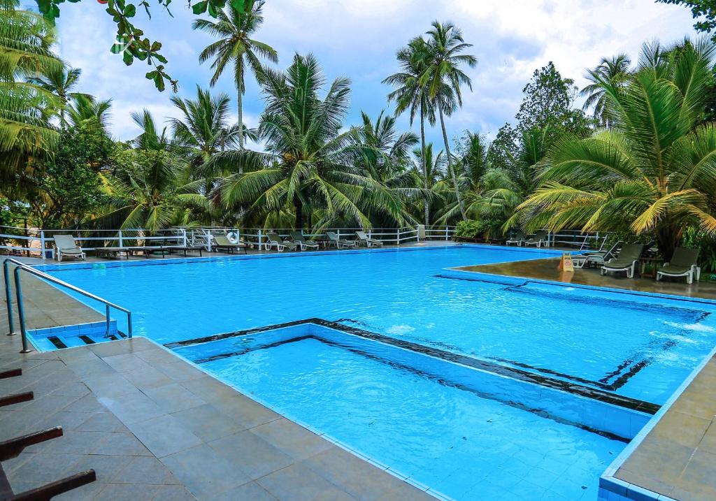 a large swimming pool with blue water and palm trees at Lagoon Paradise Beach Resort in Tangalle