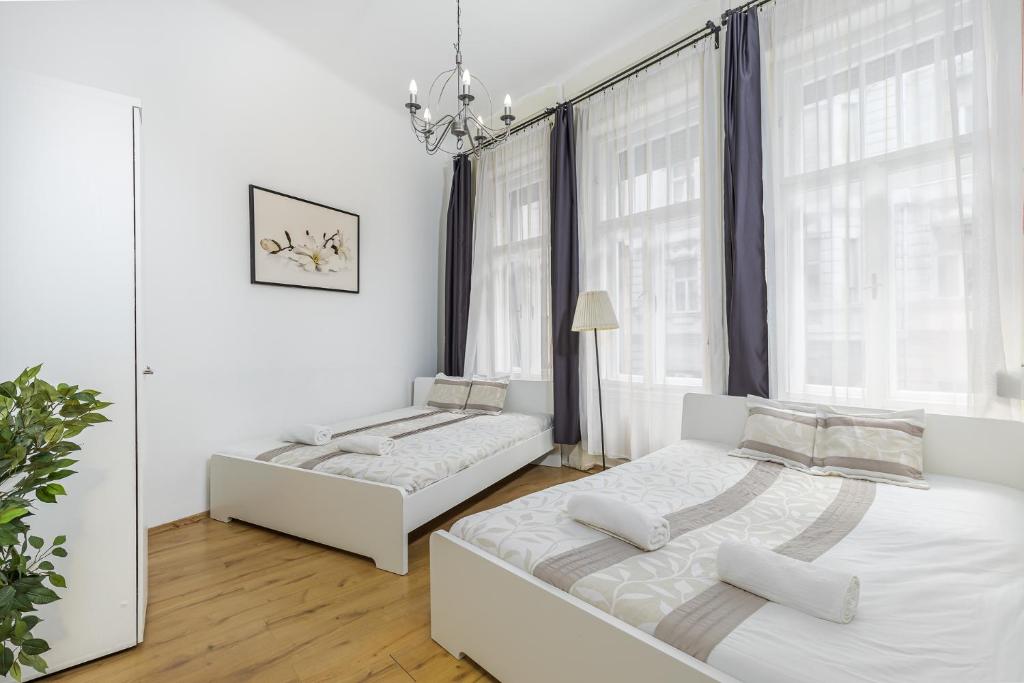 a white bedroom with two beds and a chandelier at Real Apartments Wesselényi in Budapest