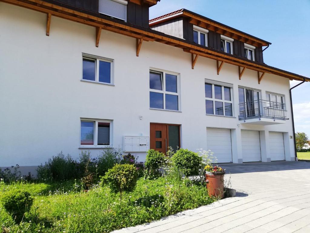 ein weißes Haus mit einem Holzdach in der Unterkunft Ferienwohnungen Weishaupt, Pfingstweider Str. 30 in Meckenbeuren