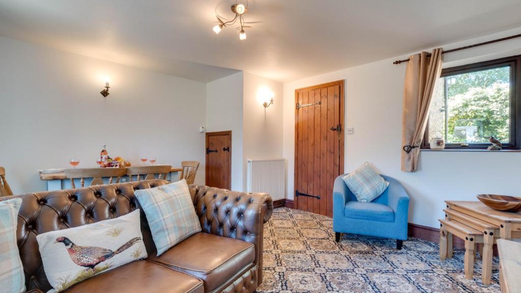 sala de estar con sofá de cuero y silla azul en Wayside Cottage en Tansley