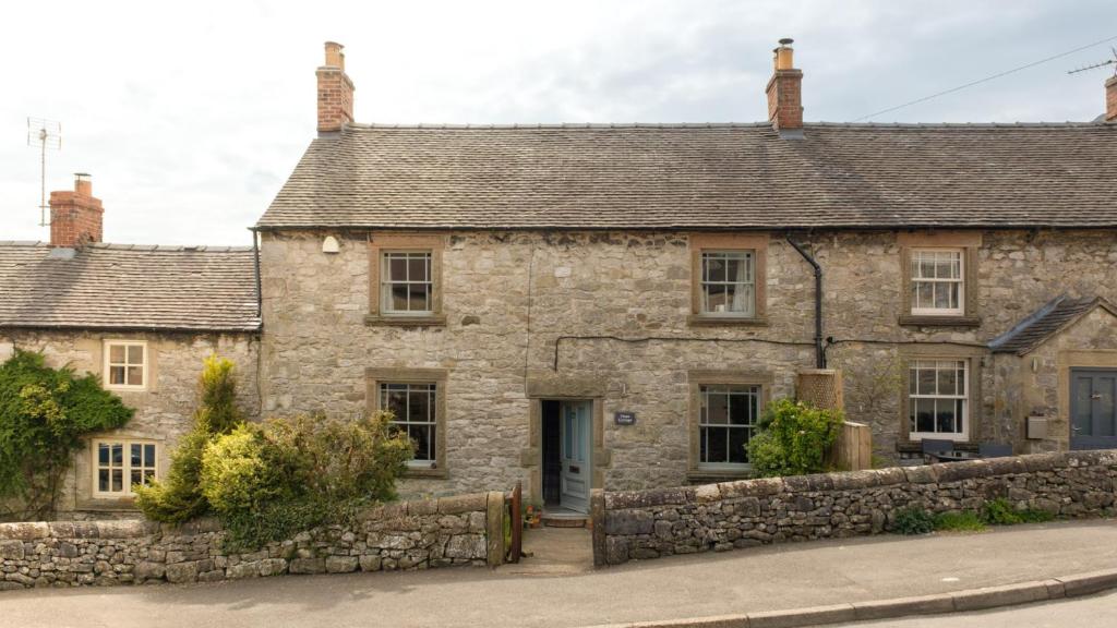 an old stone house with a stone wall at Hope Cottage in Brassington