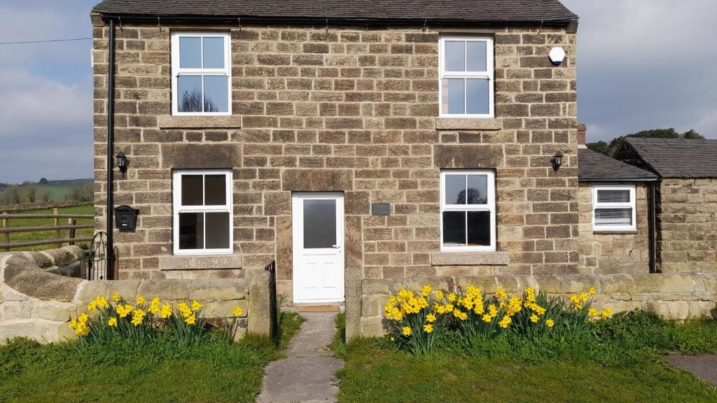 a brick house with yellow daffodils in front of it at Beau Cottage in Crich