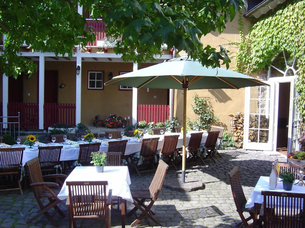 un patio con mesas, sillas y sombrilla en Hotel Agnesen-Hof en Barweiler