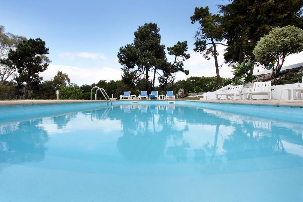 una grande piscina con acqua blu e sedie bianche di Uma Quinta na praia, vista mar a 2 passos de Lisbo a Costa da Caparica