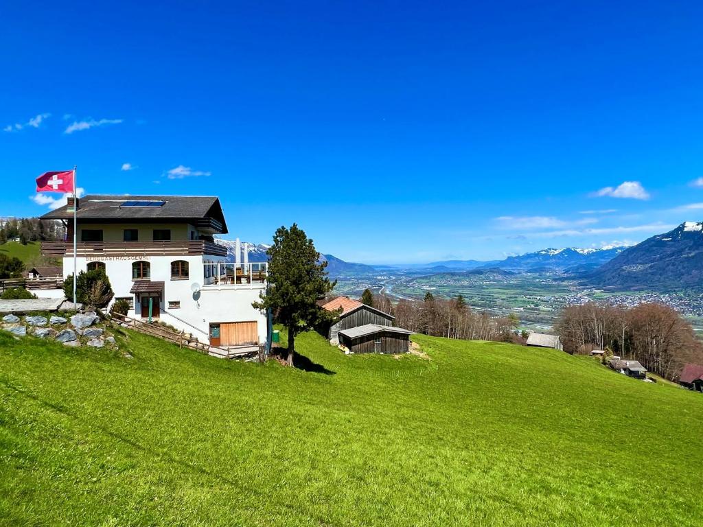 Una casa en una colina verde con una bandera. en Aparthotel-Almgasthaus Gemsli - A bisal Österreich überm Schweizer Rheintal, en Sevelen