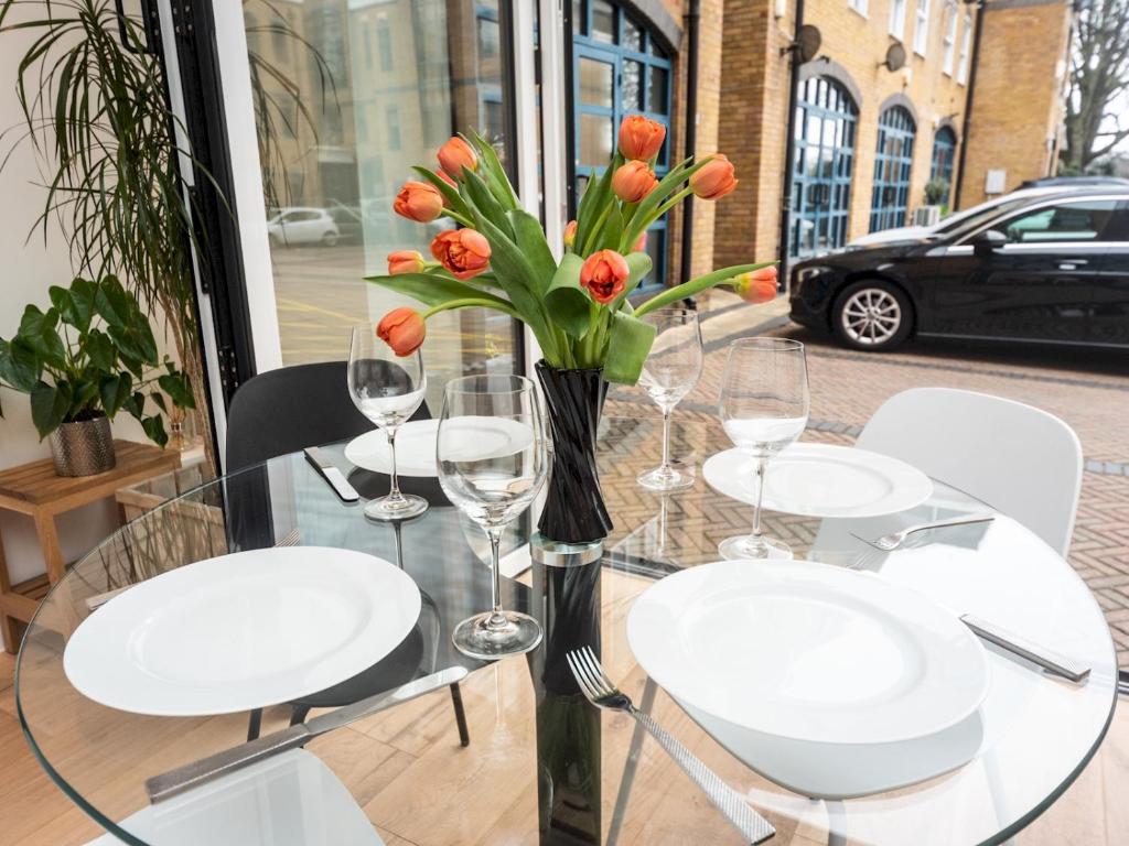 una mesa de cristal con sillas blancas y un jarrón con flores naranjas en Modern Luxury 1 Bedroom Spacious Flat, en Londres