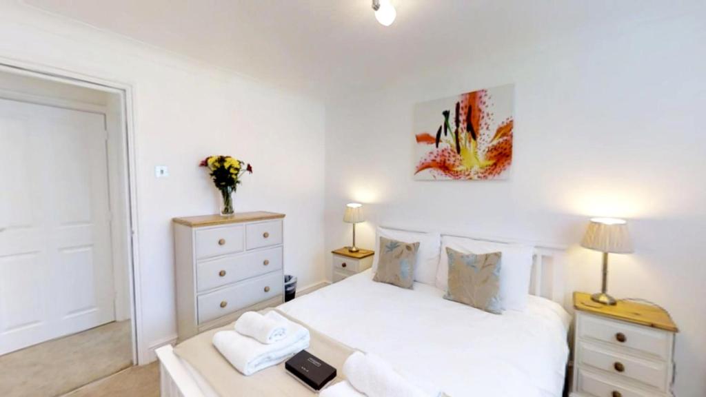 a white bedroom with a bed and a vase of flowers at Signet Apartments - Coronation House in Cambridge