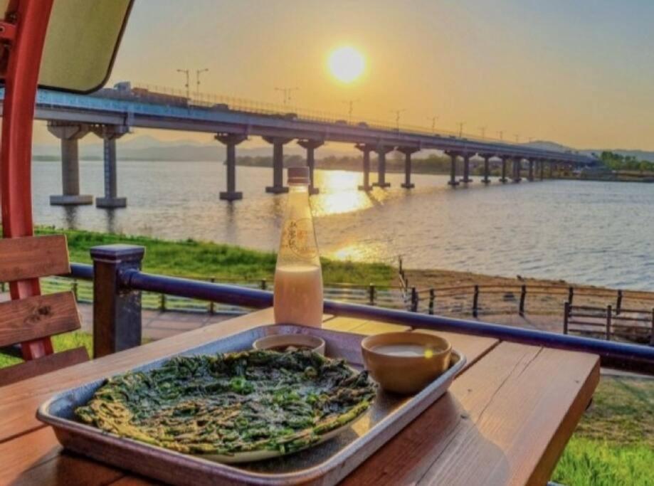 a pizza sitting on a table with a drink and a view of a bridge at Hosandong House in Daegu