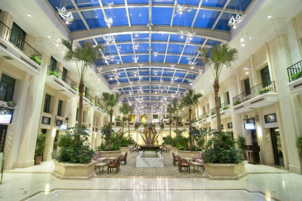 un gran vestíbulo con un techo con palmeras y una fuente en Jianguo Hotspring Hotel, en Beijing