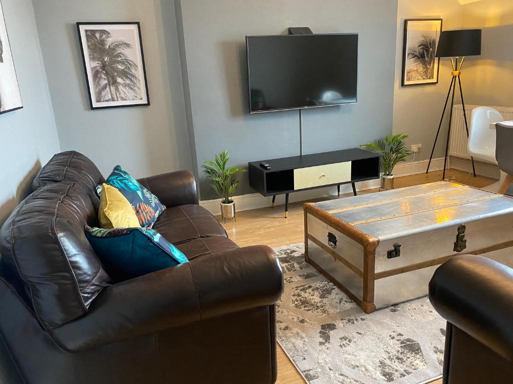 a living room with a leather couch and a flat screen tv at Aspen House - Apartment 3 in Colwyn Bay