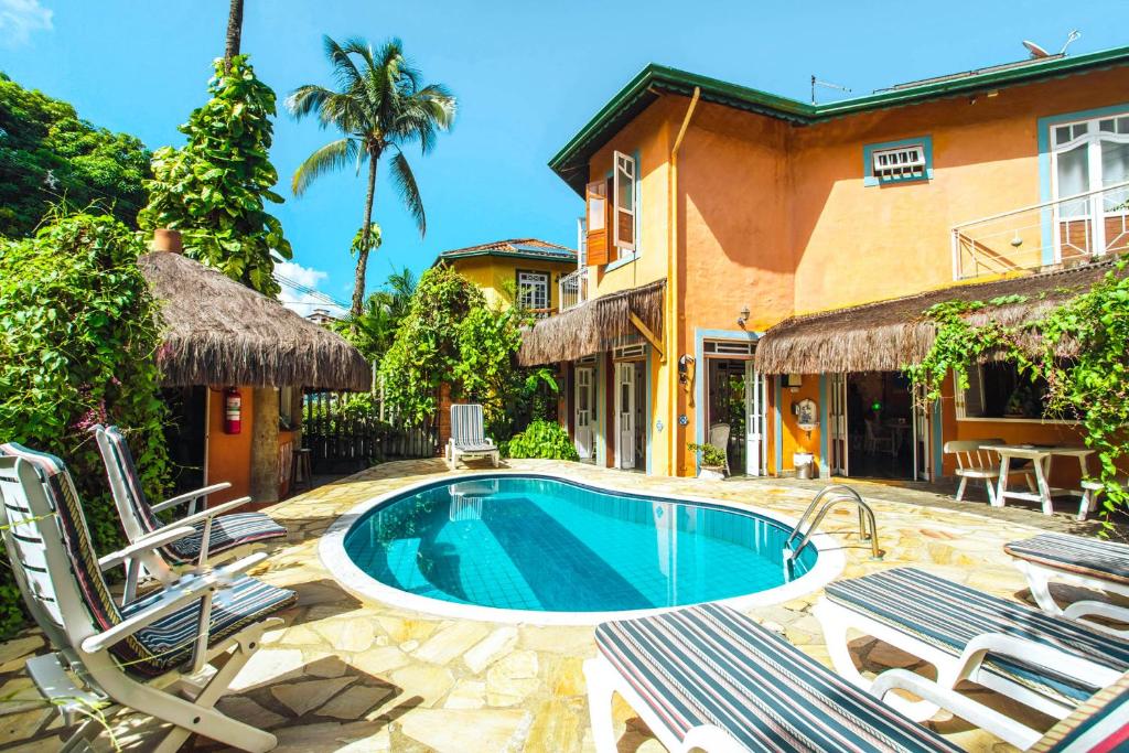 a swimming pool in a yard with chairs and a house at VELINN Pousada Ponta do Pequeah in Ilhabela